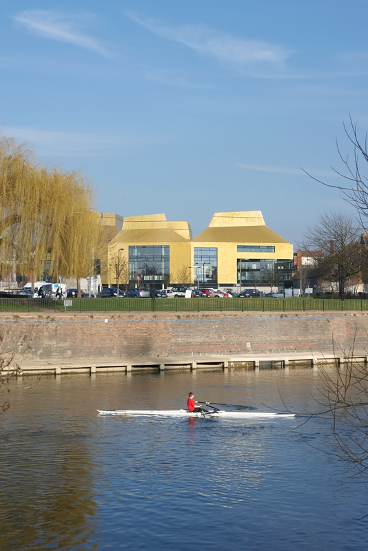 In the foreground, a child rows on the River Severn. In the background, not far from the river's edge, is The Hive.