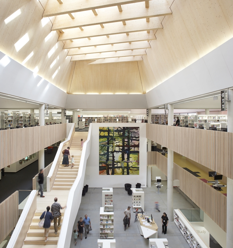 A view of the atrium of The Hive, as seen from the third floor. There are several exhibition stands, and a help desk without chairs. Lots of natural light falls from the large skylight above. A long staircase connects the three floors.